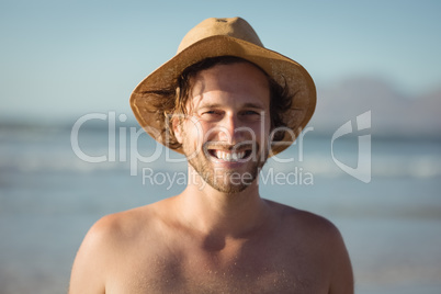 Portrait of happy shirtless man wearing hat at beach