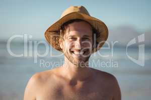 Portrait of happy shirtless man wearing hat at beach