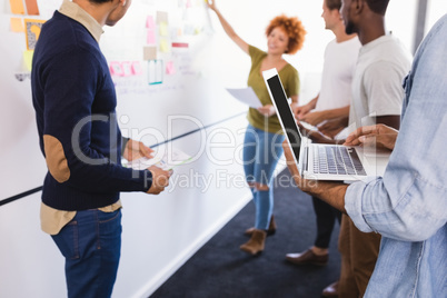 Colleagues standing by businesswoman explaining plan on whiteboard
