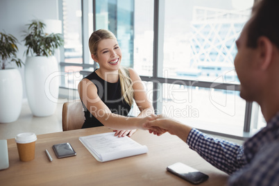 Smiling executives shaking hands at desk