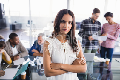 Portrait of young businesswoman standing with team working in background