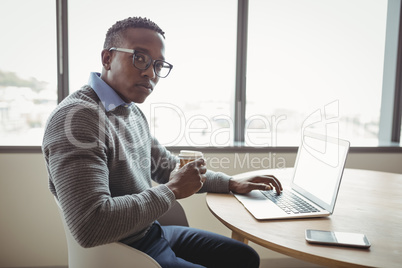Portrait of confident executive having coffee while using laptop