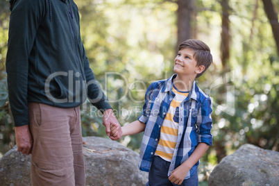 Mid section of father holding hand of boy in forest