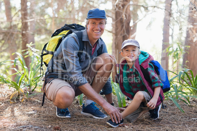 Portrait of father tying shoelace for son in forest