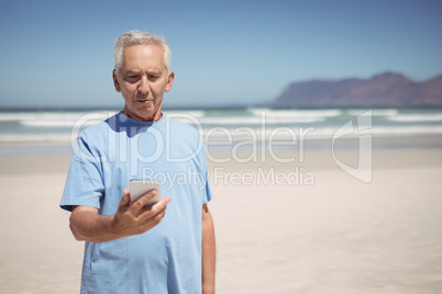 Senior man holding mobile phone at beach