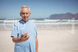 Senior man holding mobile phone at beach