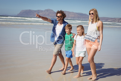 Happy man pointing away with family walking at beach