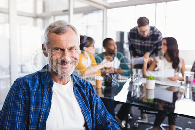 Portrait of smiling businessman with team working in background