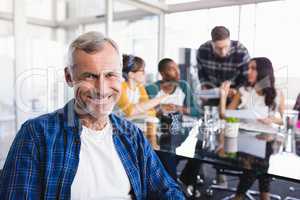 Portrait of smiling businessman with team working in background