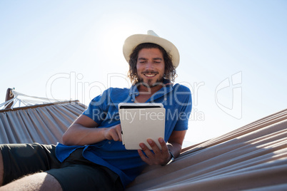 Happy man using digital tablet on hammock at beach