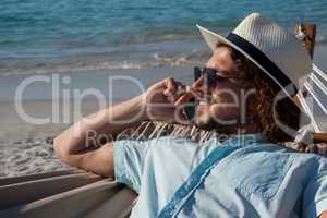 Man relaxing on hammock and talking on mobile phone on the beach