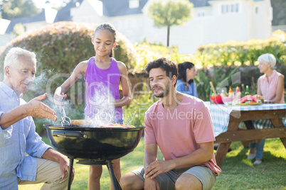 Father and grandfather watching while girl preparing barbecue