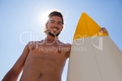 Smiling surfer with surfboard standing against blue sky