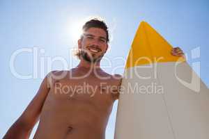 Smiling surfer with surfboard standing against blue sky
