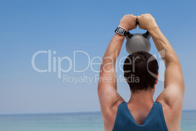 Rear view of man lifting kettlebell at beach