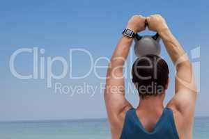 Rear view of man lifting kettlebell at beach