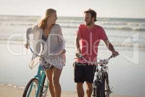 Happy couple with bicycles walking at beach