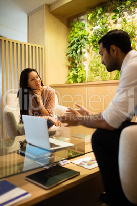 Business colleagues discussing while sitting on sofa by laptop on table