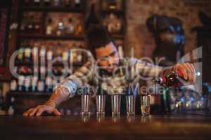 Waiter pouring tequila into shot glasses at counter