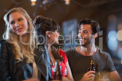 Smiling friends looking at each other while holding beer bottles`
