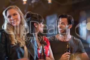 Smiling friends looking at each other while holding beer bottles`