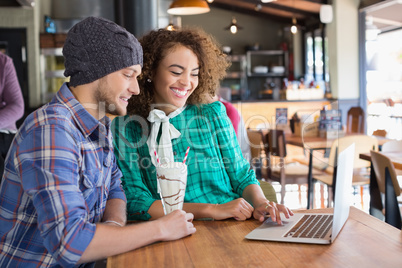 Happy friends using laptop at table in restaurant