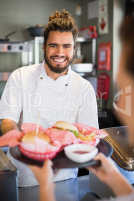 Happy chef giving burgers to waitress