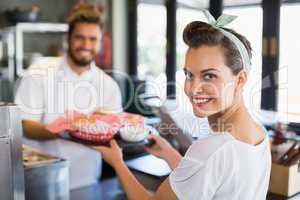 Portrait of waitress taking plate from chef in kitchen