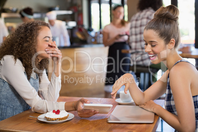 Female friends looking into tablet and laughing while sitting in restaurant