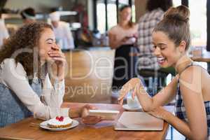 Female friends looking into tablet and laughing while sitting in restaurant
