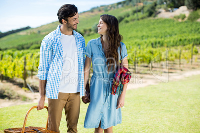 Happy couple looking at each other with holding picnic blanket and basket