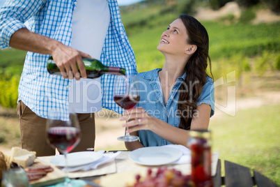 Smiling woman looking at man pouring red wine in glass