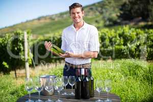 Portrait of man holding wine bottle by table at vineyard