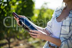 Mid section woman holding wine bottle at vineyard