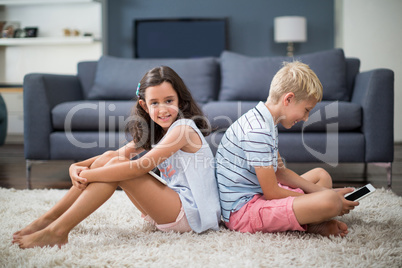 Siblings sitting back to back while boy using digital tablet