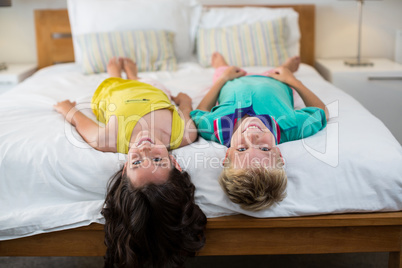 Portrait of smiling siblings lying on bed in bedroom