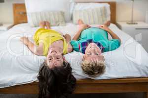 Portrait of smiling siblings lying on bed in bedroom