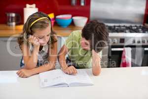 Siblings reading book in kitchen