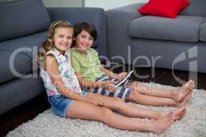 Portrait of siblings using digital tablet in living room