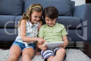 Siblings using digital tablet in living room