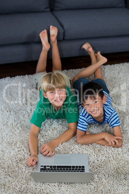 Portrait of smiling siblings with laptop lying on rug