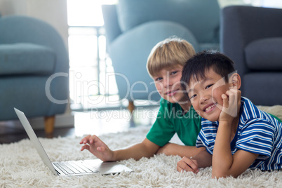 Portrait of siblings lying on rug and using laptop in living room