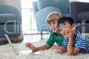 Portrait of siblings lying on rug and using laptop in living room