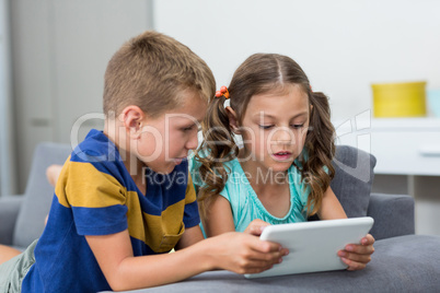 Siblings using digital tablet in living room