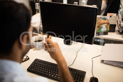 Businessman holding coffee cup by desktop pc in office