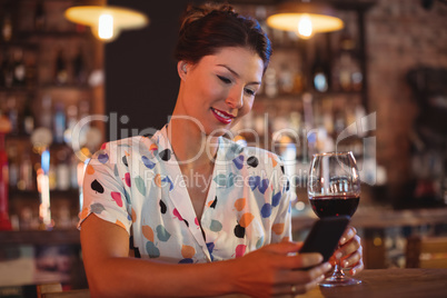 Young woman using mobile phone while having wine