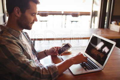 Man holding mobile phone while using laptop