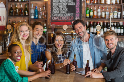 Portrait of cheerful young friends with beer bottles in pub