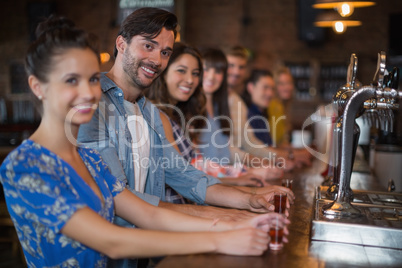 Happy friends holding short glasses on counter in bar