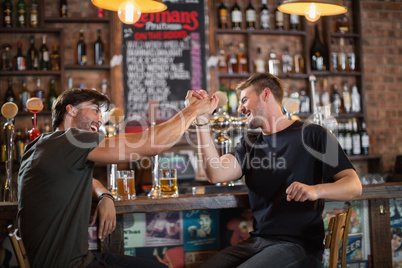 Male friends giving high five while sitting in bar